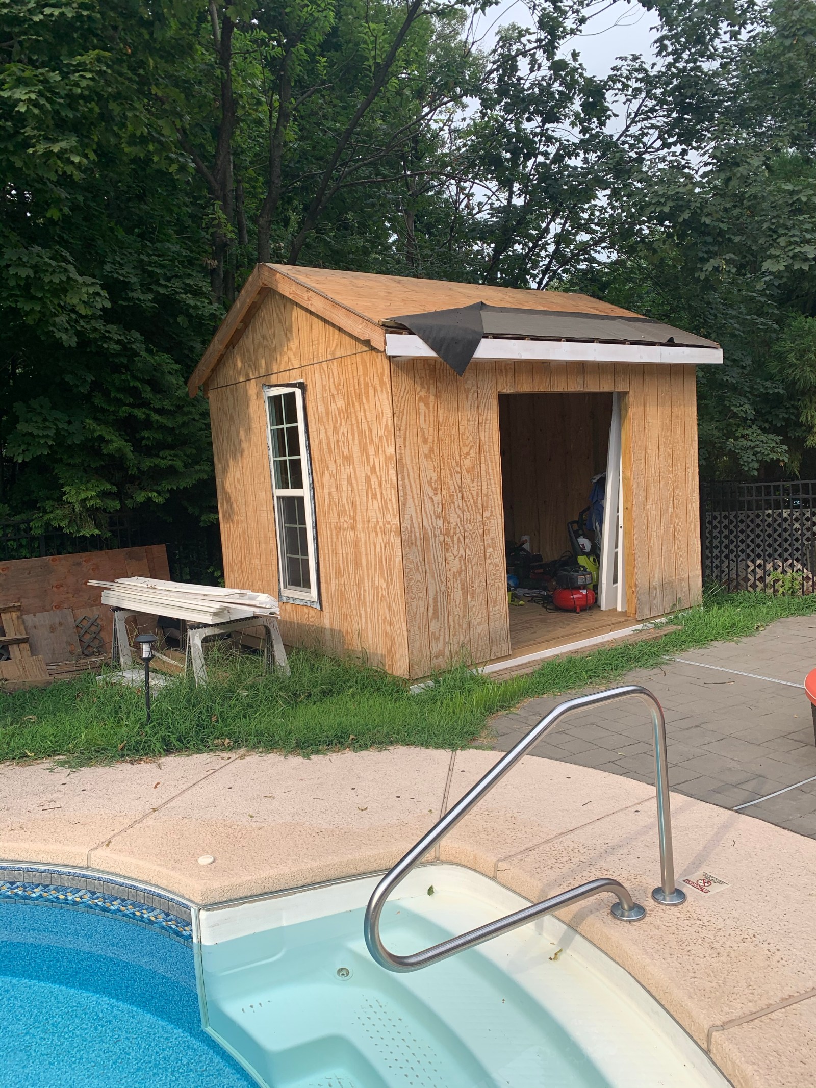 A small gabled wooden shed beside a backyard pool