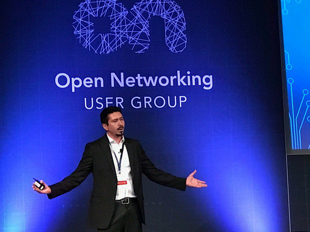 Truman speaking on stage in front of an Open Networking User Group backdrop