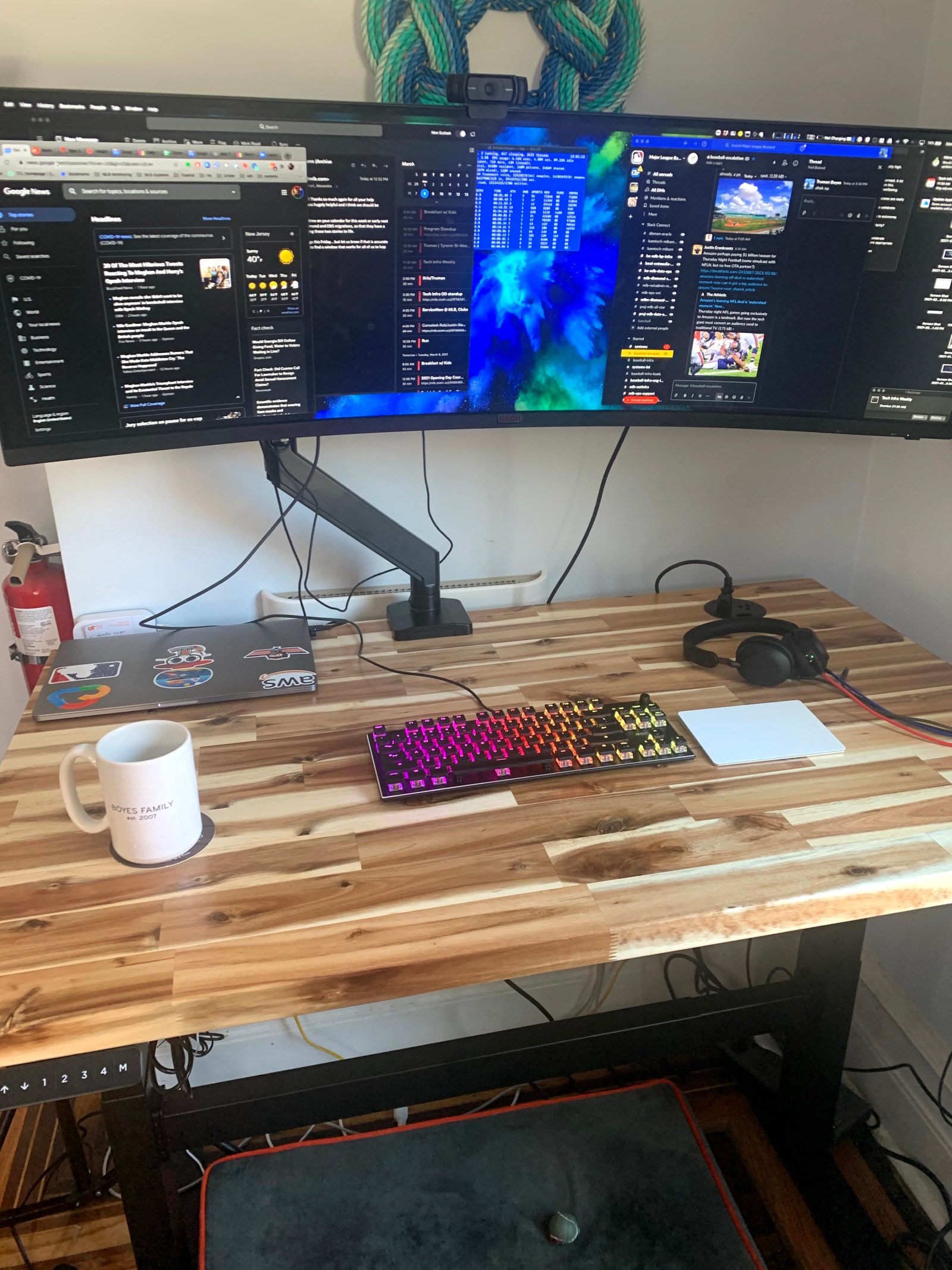 A standing desk with a wide curved monitor, keyboard and coffee mug